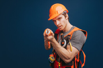 Builder holds construction adhesive and aims at the camera, isolated over blue background