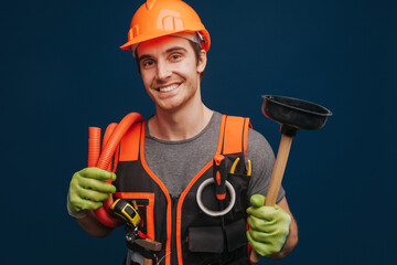 Happy builder is holding plunger and trumpet, isolated over blue background