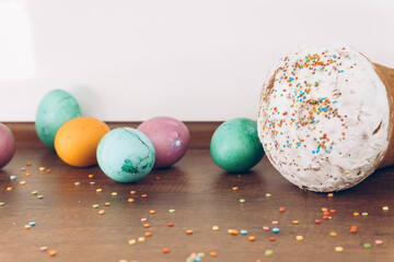 Easter cake with scattered sprinkles on a wooden table, and Easter eggs of different colors - yellow eggs, green and purple eggs. Easter eggs and cake with scattered sweets.