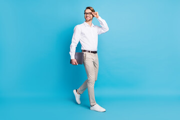 Fototapeta na wymiar Full body photo attractive positive young man walk smile businessman look empty space hold laptop isolated on blue color background
