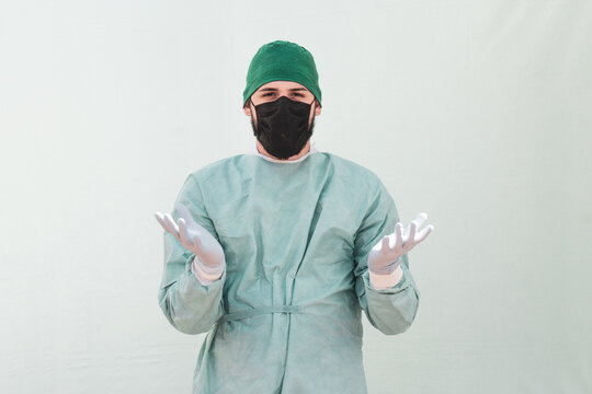 Male surgeon in a facemask and antibacterial gloves in a confused pose isolated on light background
