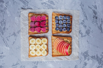 Toasted sandwich bread with peanut butter, banana, frozen berries raspberries, blueberries. Served on concrete background. Healthy, balanced traditional breakfast. Vegan sweet dessert, top view