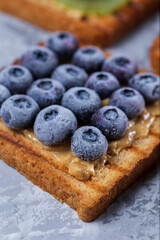 Toasted sandwich bread with peanut butter, frozen berries raspberries, blueberries. Served on concrete background. Healthy, balanced traditional breakfast. Vegan sweet dessert, top view