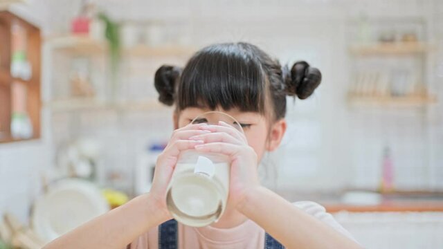 Portrait of Asian little young girl drinking milk in the kitchen.