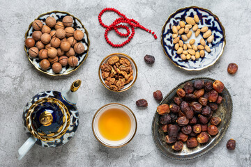 Popular food during Iftar - macadamia nuts, pistachios, walnuts, dry dates. Karan, rosary, teapot, bowl with black tea on concrete background Top view Flat lay Muslim holiday of holy month of Ramadan