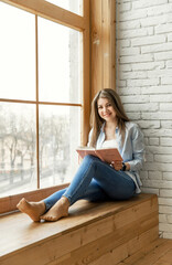 young girl student sitting by the window holding a diary and a pen. Beautiful female hands writing an entry in the diary with an ink fountain pen.