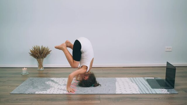 Caucasian girl does yoga in front of a laptop Child does a headstand Girl does gymnastic exercises Gymnastics Online Yoga at home