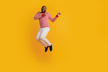 Handsome man jumping direct fingers empty space on yellow background