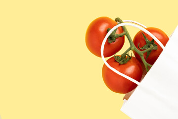 White paper bag with tomatoes on yellow background, place for text,top view