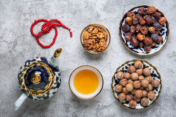 Fototapeta na wymiar Popular food during Iftar - macadamia nuts, pistachios, walnuts, dry dates. Karan, rosary, teapot, bowl with black tea on concrete background Top view Flat lay Muslim holiday of holy month of Ramadan