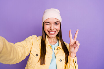 Photo portrait of smiling girl taking selfie in casual clothes showing v-sign gesture winking isolated on pastel violet color background