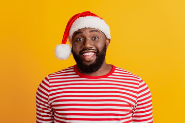 Portrait of guy in santa hat toothy beaming smile on yellow wall