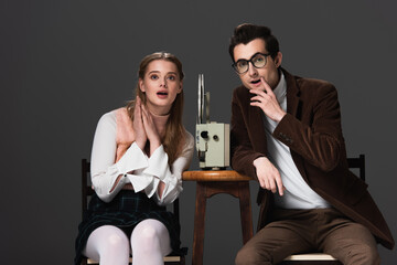 worried couple watching movie on vintage film projector while sitting isolated on black