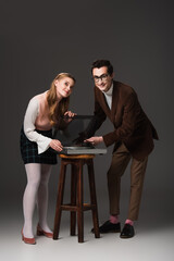 Obraz premium full length view of happy couple in retro outfit near record player on dark grey background