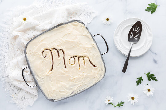 Top down view of a cake with the word Mom carved in the cream cheese frosting, ready for serving. A Mother's Day concept