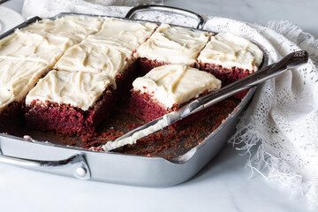 Close up of a baking pan filled with red velvet chocolate brownie squares topped with cream cheese...