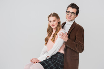 happy man in brown blazer hugging smiling girlfriend isolated on grey