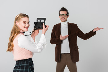 cheerful man pointing with hands near pretty woman with vintage camera isolated on grey, blurred background