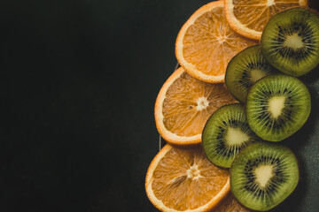 orange and kiwi slices lie on a gray plate, which stands on a black background