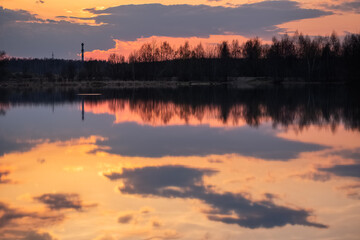 Fototapeta na wymiar Dramatic sunset sky, clouds reflect in still water surface of forest lake