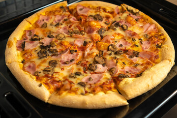 Delicious mouth-watering round pizza with bacon, mushrooms, tomatoes and cheese on a baking sheet close-up