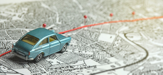 City map, route marked with safety pins. A blue toy car is driving along the road. Concept: journey...
