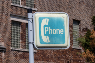Sign for an ancient pay phone. Before cell phones in the 20th and early 21st centuries, people were forced to use pay phones to call others when they were away from home.