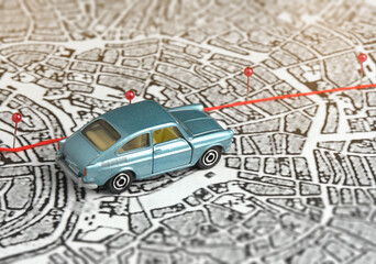 City map, route marked with safety pins. A blue toy car is driving along the road. Concept: journey along the route, destination, goal.