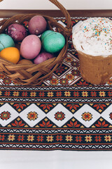 Ukrainian embroidered shirt and Easter cake on a wooden table with Easter eggs of different colors - yellow eggs, green and purple eggs in a basket.Easter eggs and Easter cake on an embroidered towel.