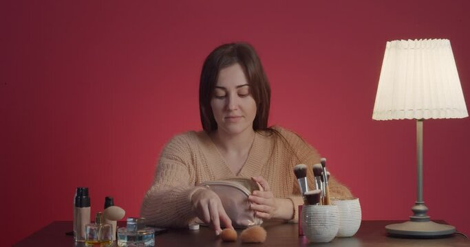 Young woman taking cosmetics and brushes from bag at table