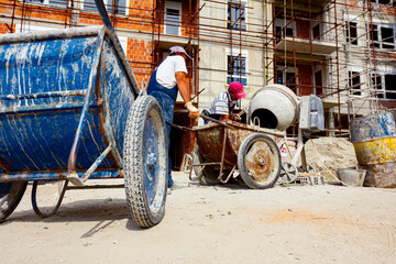 Fototapeta na wymiar Workers are pouring concrete from cement mixer into wheelbarrow