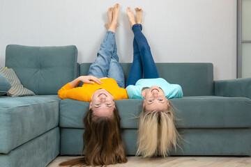 Two happy young female sisters are lying on the sofa with their legs up and their hair down....