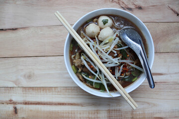 Beef noodles with stainless spoon and chopsticks in the bowl, Thai delicious food isolated on wooden background closeup.