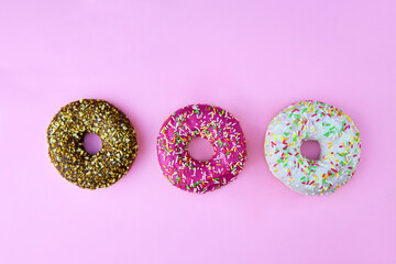 Three colorful donuts on a pink background. Top view.