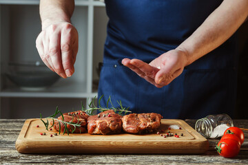 Chef hands cooking meat steak. Chef adding salt and pepper on raw meat. Man cooking meat steak on kitchen.