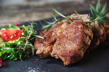 Grilled beef steaks on black stone slate. Tasty juicy grilled steak and salad with tomatoes. Main course beef dinner.