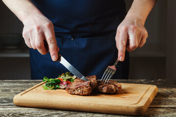 Chef cutting grilled beef steak on wooden board. Juicy grilled beef steak with spices on cutting board.