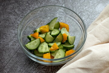 
Fresh vegetable salad of green cucumber and yellow pepper in a bowl on a table with textiles
