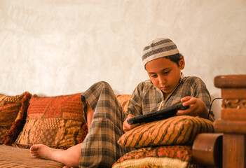 A boy of 8 years in Moroccan national clothing - djellaba, plays in the console.