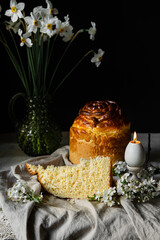 Homemade Ukrainian traditional Easter bread -- paska, natural bee wax candles and white spring flowers on linen tablecloth on dark background.