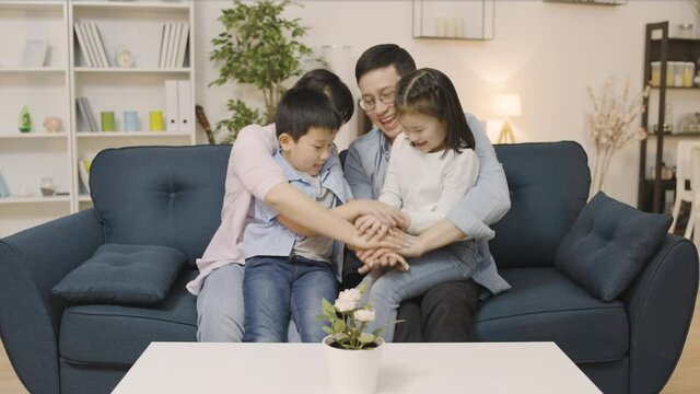 Cheerful asian family with two kids stacking hands, happy together at home