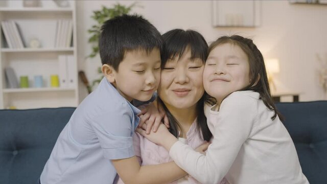 Sweet asian kids kissing mother on cheeks, parent and child relationship, family