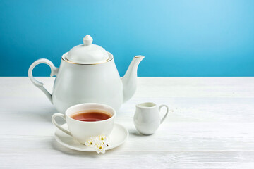 A cup of tea, a teapot and a milk jug on a white table.