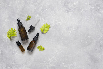 Bottles of dark amber glass with essential oil and face cream on a gray concrete background. Natural SPA organic cosmetic. Layout of the beauty salon branding. Flat lay, top view.