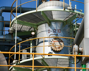 Petrochemical plant. Close-up of oil refinery column (distillation tower) and pipes on blue sky..