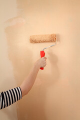 Closeup of young worker hand painting wall in a house to orange color using paint roller