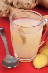 Infusion de gingembre frais dans un mug en gros plan sur fond rouge