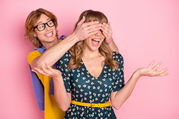 Portrait of attractive cheerful couple guy closing girl's eyes having fun celebrate good mood isolated over pink pastel color background