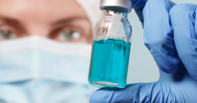 Caucasian female doctor in protective gloves and mask holding glass ampoule vial with medicine or vaccine against diseases, coronavirus