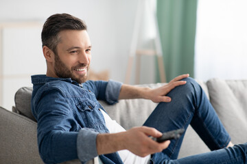 Fototapeta premium Relaxed bearded man switching channels on TV